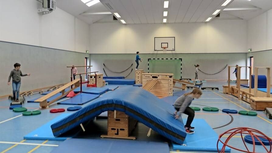 Children engaging in gymnastics and physical activities on various equipment in a large indoor gymnasium.