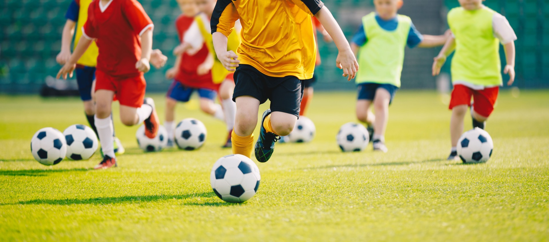 Fußball-Trainingslager. Fußball Kinder Trainingskurs. Kinder, die auf dem Rasenplatz Fußball spielen. Gruppe von Schulkindern, die Fußbälle laufen und treten