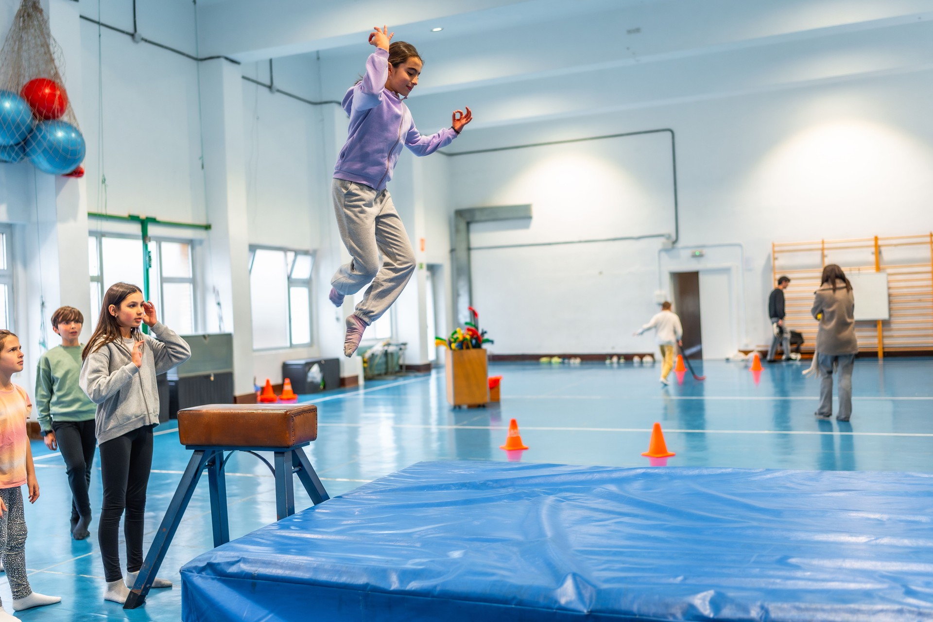 Mädchen im Grundschulalter springt im Sportunterricht über Sprungkasten