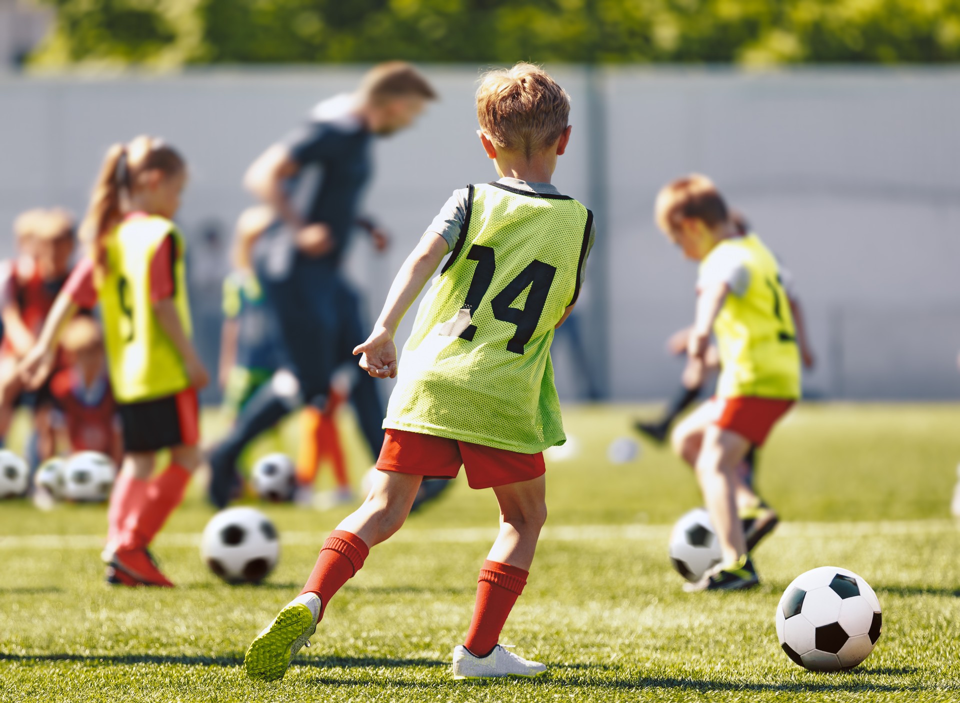 Schulkinder spielen Fußball-Fußball-Trainingsspiel mit Trainer. Kinder, die Sportbälle auf dem Rasenplatz kicken. Fußballtraining für Jugendliche